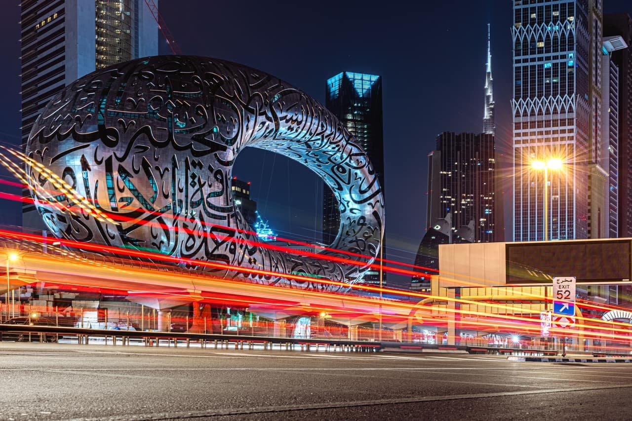 The Museum of the Future's calligraphy-clad torus lit up at night on Sheikh Zayed Road, with traffic light trails and the Burj Khalifa rising behind the Dubai skyline