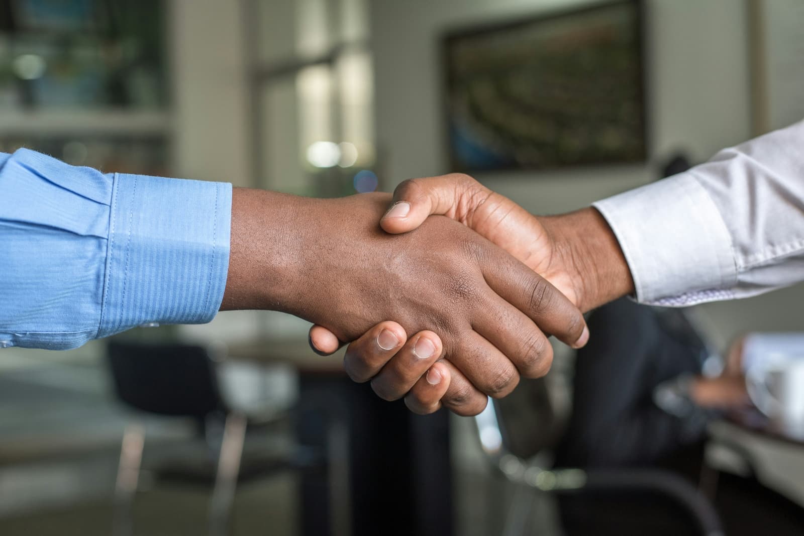 Two people shaking hands across a desk in an office